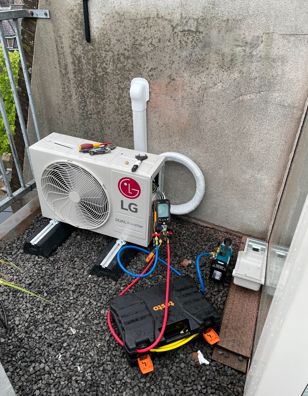 LG airco-buitendeel op een balkon, met meetapparatuur tijdens de installatie