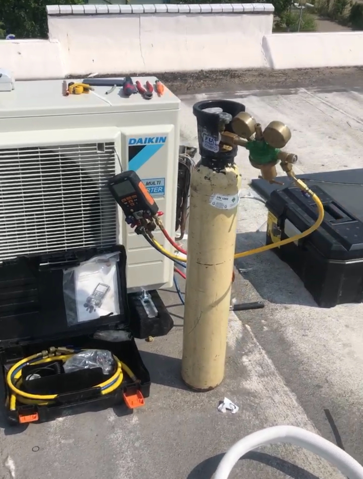 Daikin airco-buitendeel op een dak, met een gasfles, drukregelaar en digitale meetset aangesloten