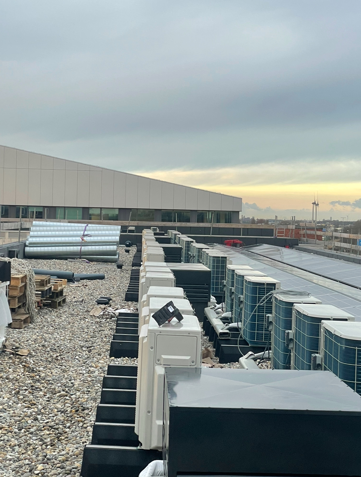 Lange rijen airco-buitendelen op een groot plat dak bij zonsondergang