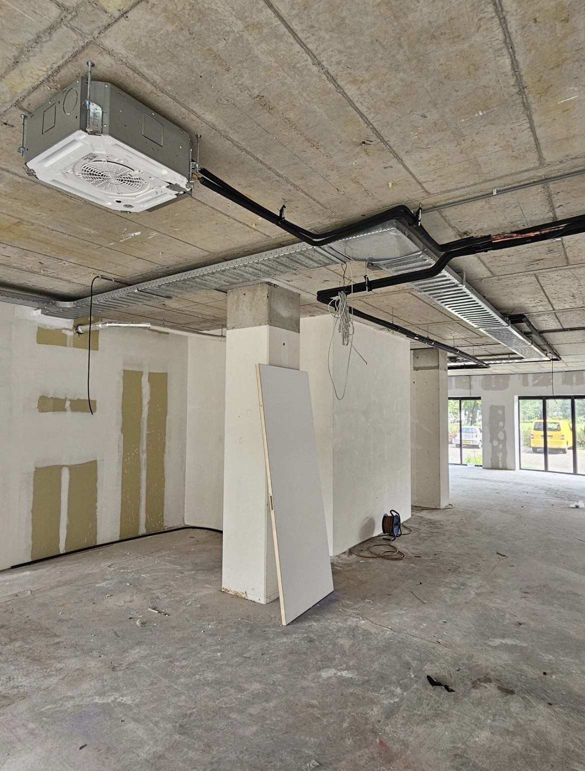 Plafondcassette-unit gemonteerd in een kantoorruimte in afbouw met betonplafond en kabelgoten